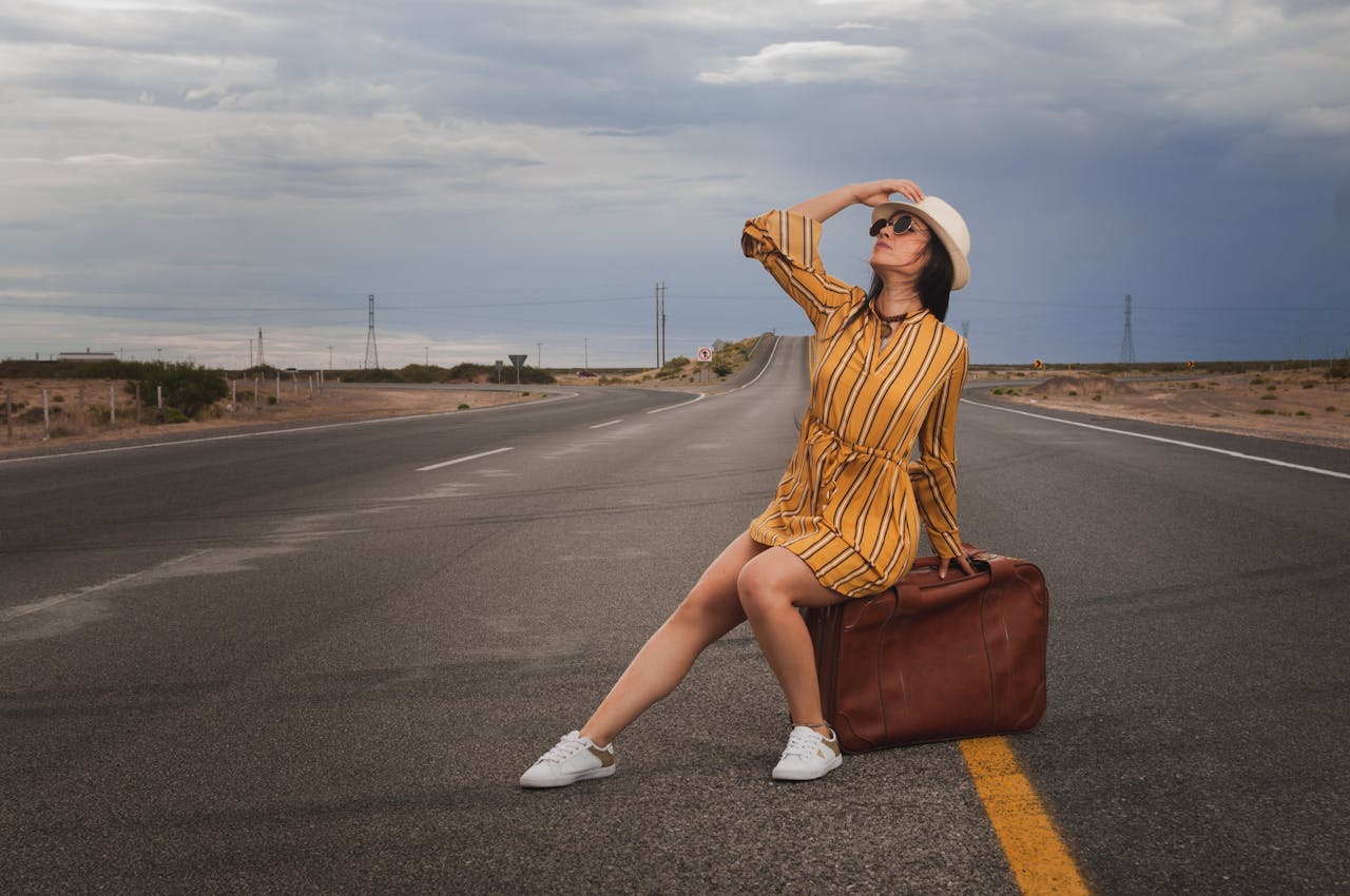 Captivating image of a woman sitting on a suitcase on a highway, embodying adventure.