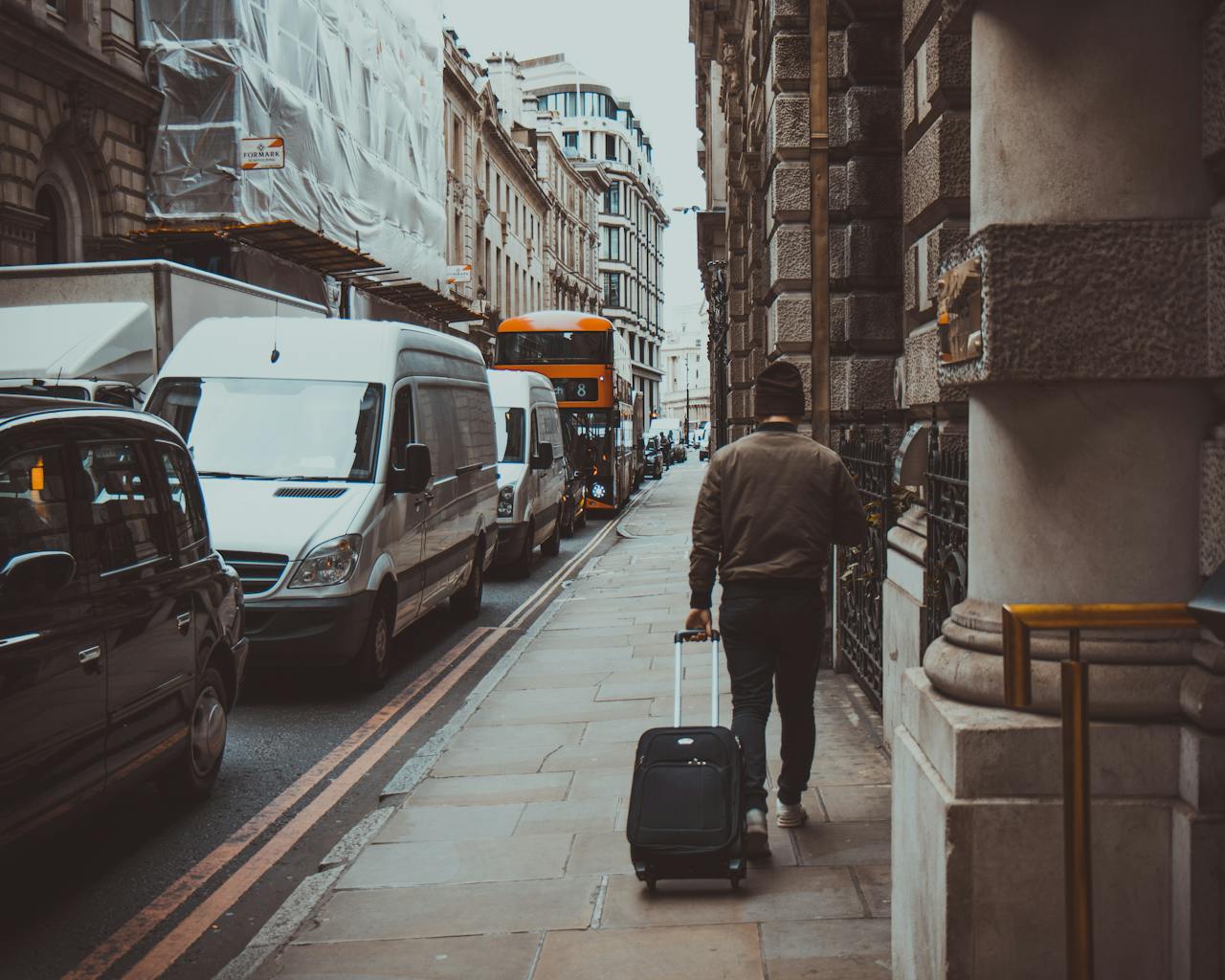 Person pulling luggage along a busy street in an urban setting with traffic and buildings.