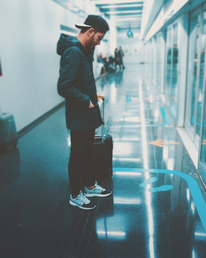 A young man with luggage waits in a sleek airport hallway, reflecting modern travel themes.